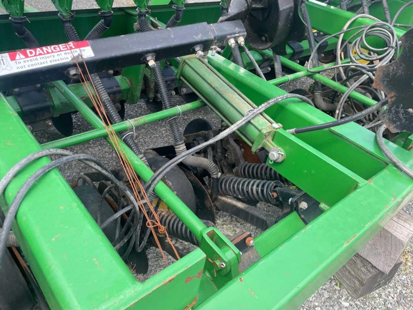 Green agricultural machine with exposed springs, hoses, and metal frame components.