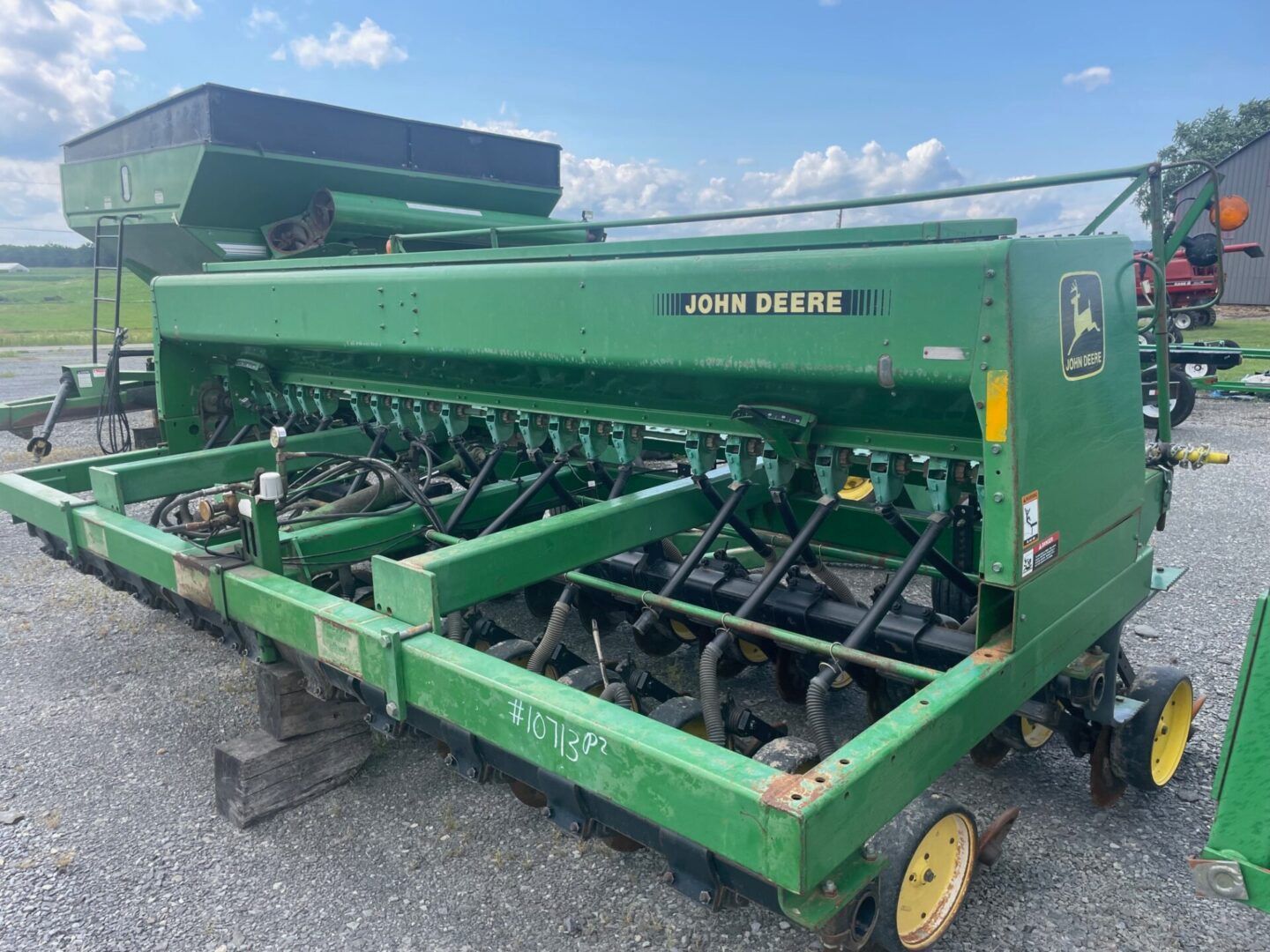 Green John Deere seed drill parked on pavement under a blue sky