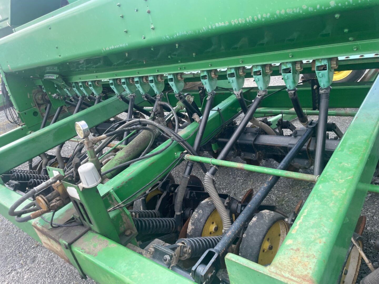 Close-up of green farm machinery with hoses, chains, and metal parts inside the frame