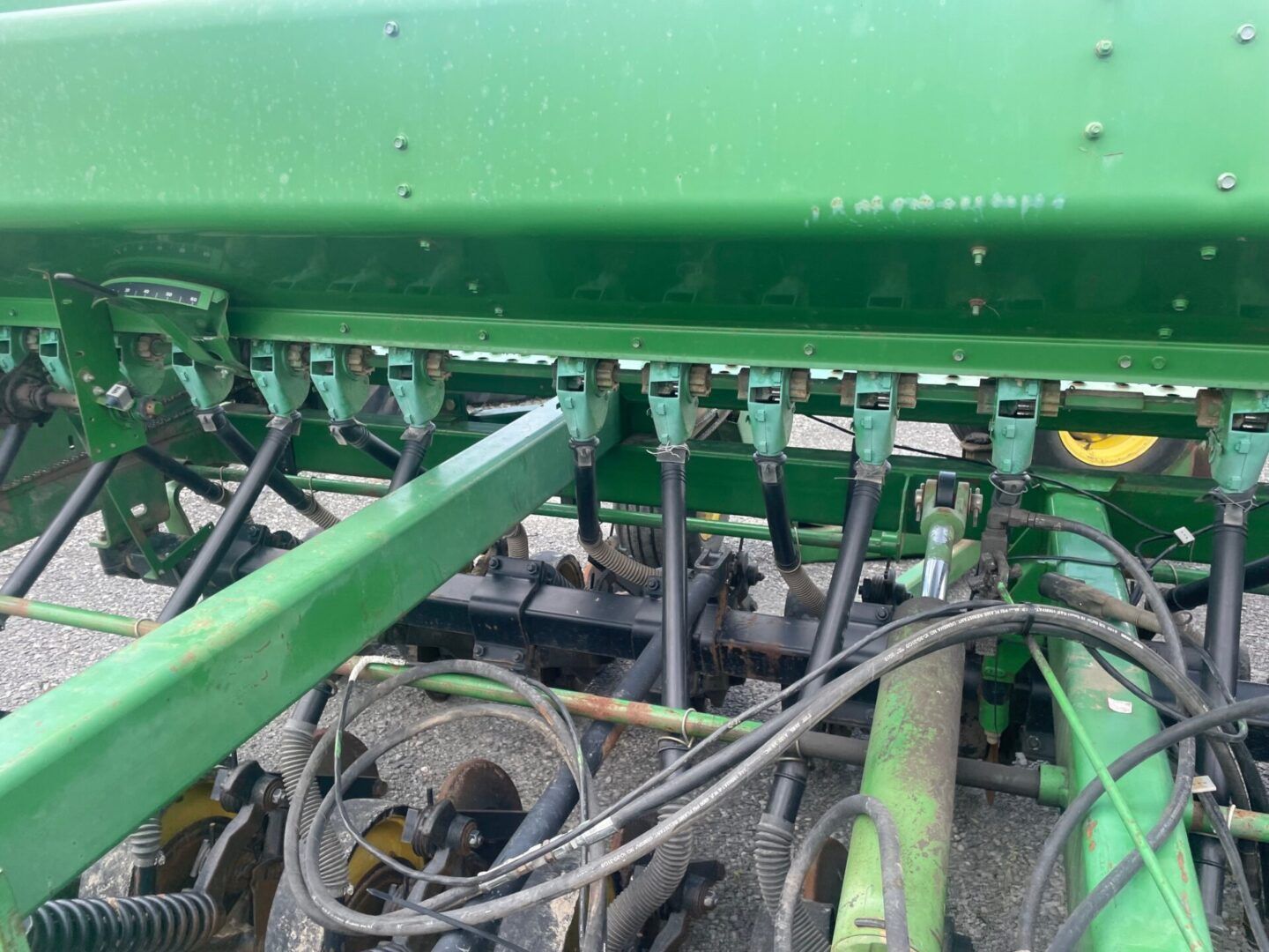 Green agricultural implement with hoses and mechanical parts, close-up in a field