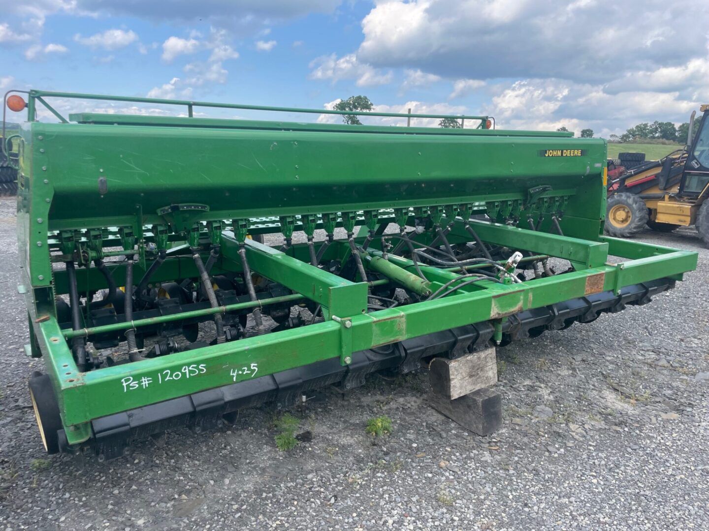 Green farm implement with multiple tines parked on gravel outdoors.