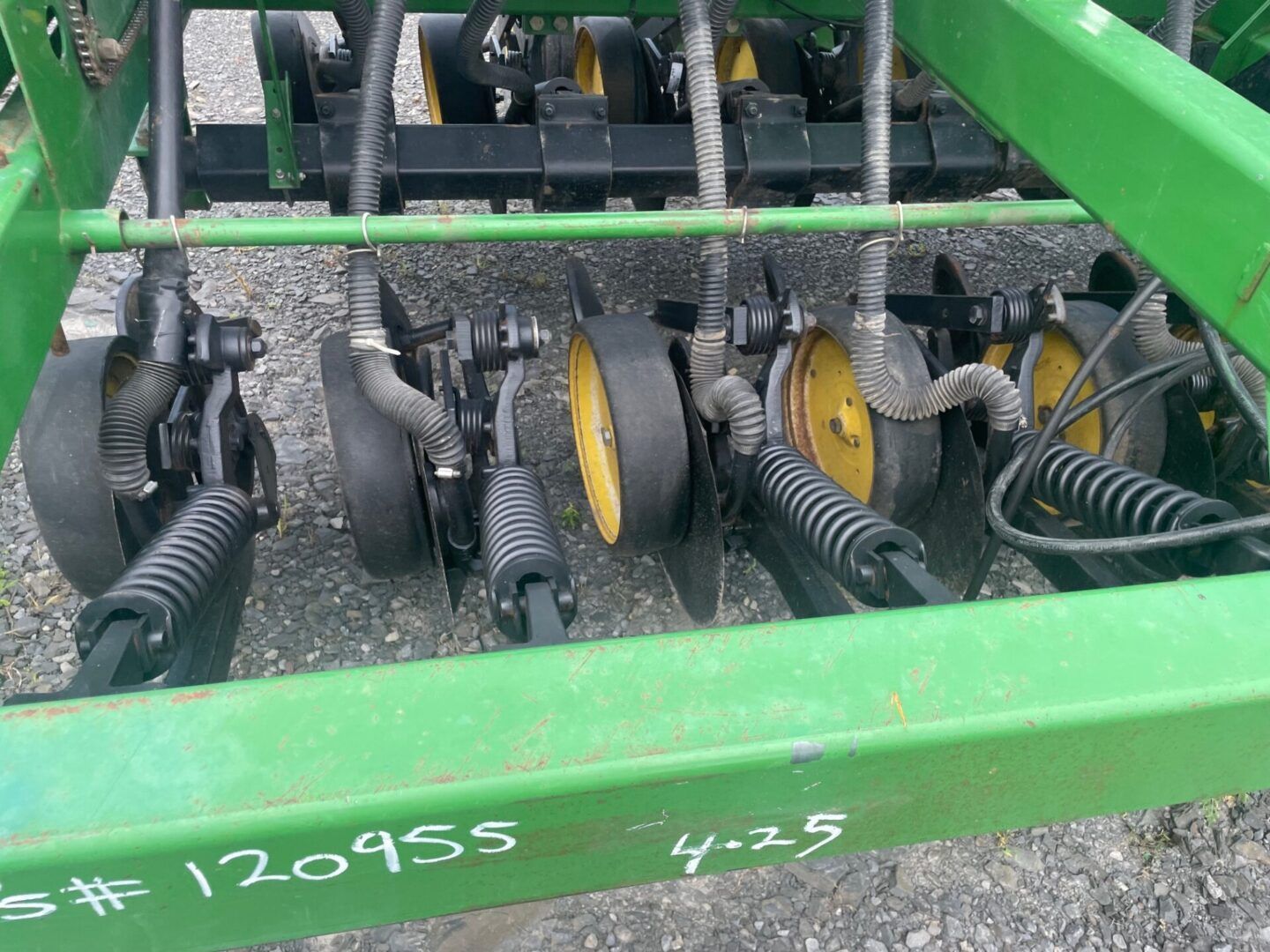 Green farm machine with rows of yellow and black rotating tines on gravel ground