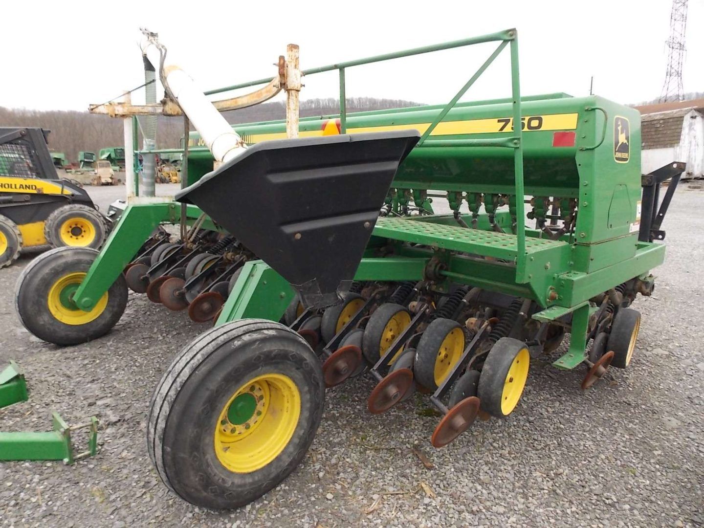 Green John Deere seed drill with yellow wheels parked on gravel lot