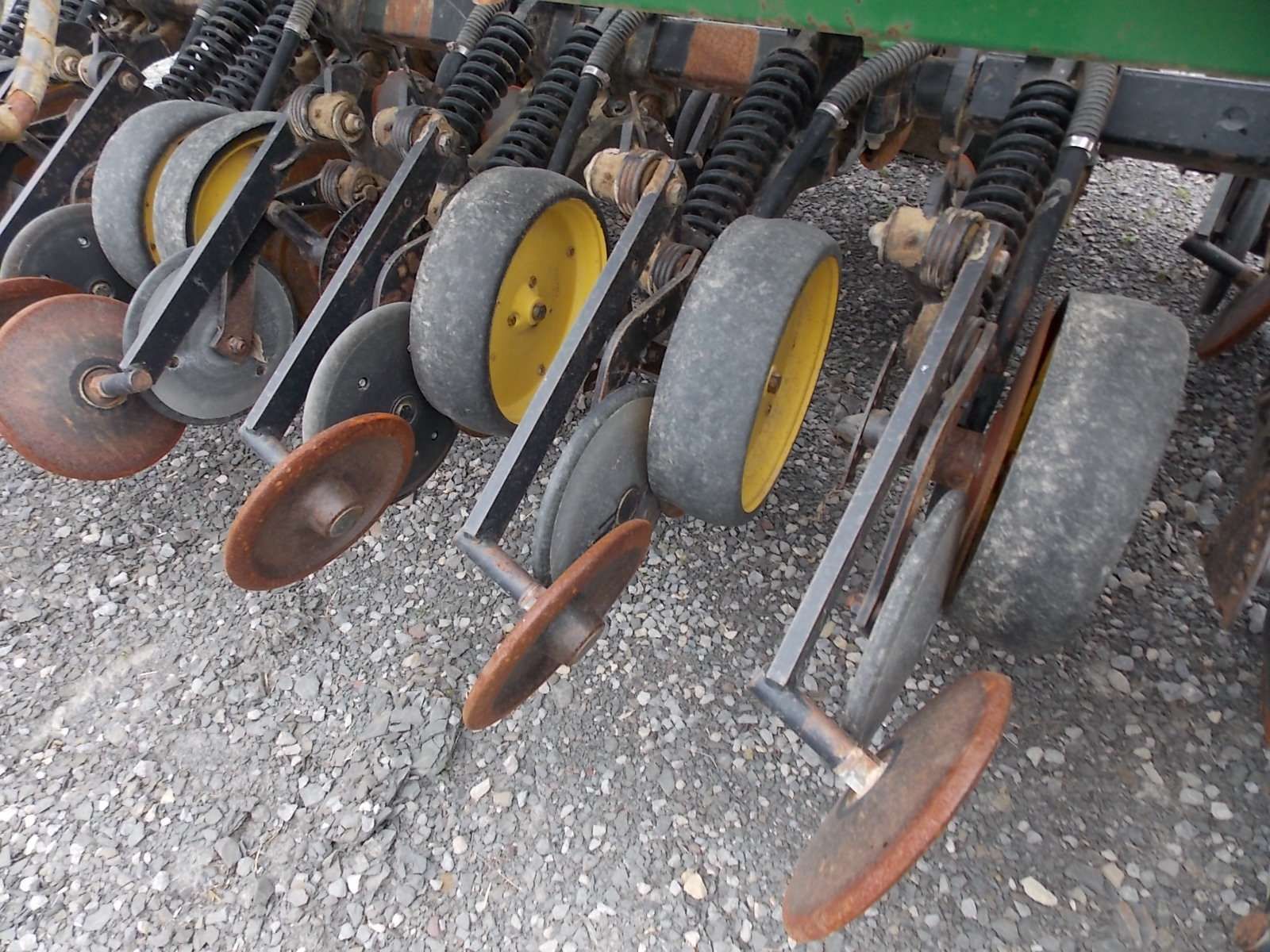 Row of farm tillage discs and wheels on gravel, with metal frames and yellow tires