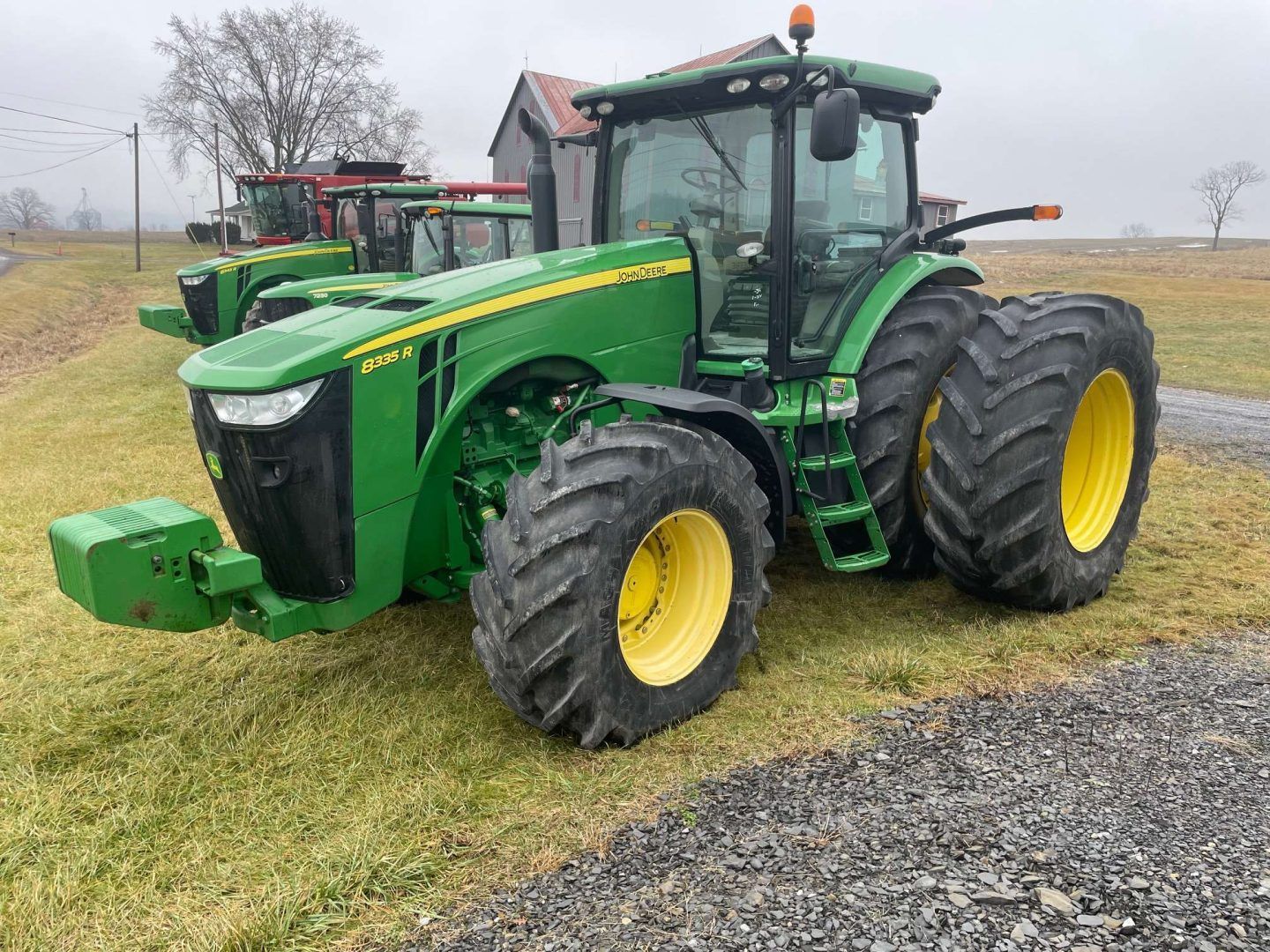 Green John Deere tractor with dual rear wheels parked on a grassy field beside gravel, overcast day