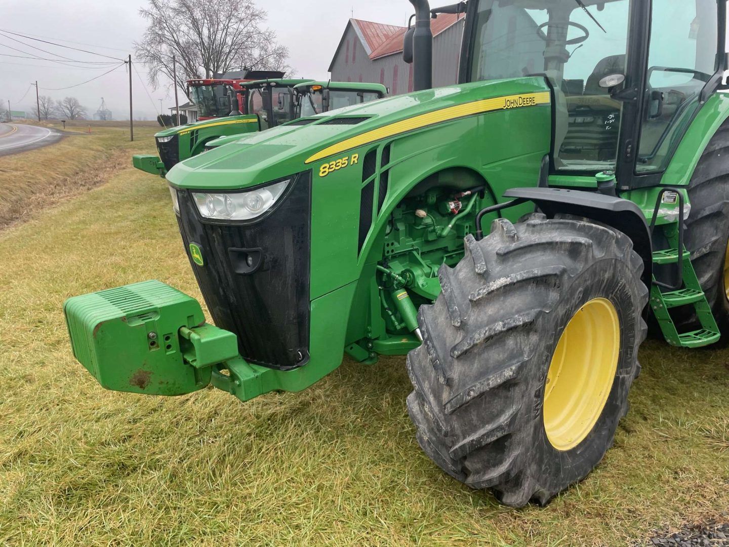Green John Deere tractor parked on a grassy roadside field on an overcast day