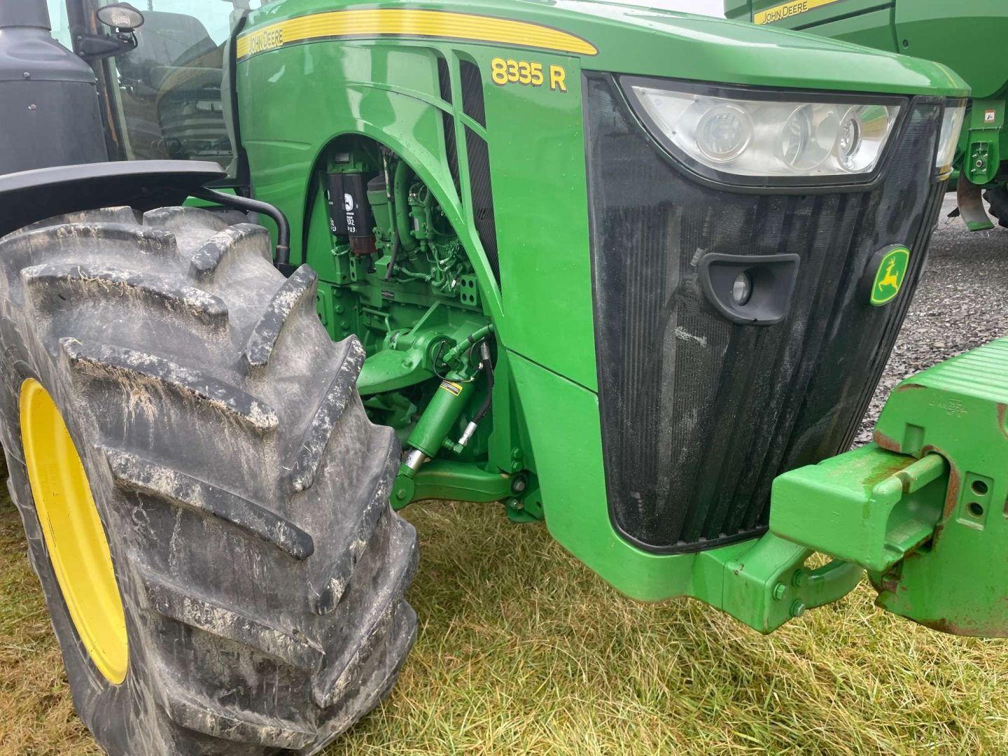 Close-up of a green John Deere tractor’s front wheel and hood on grass.