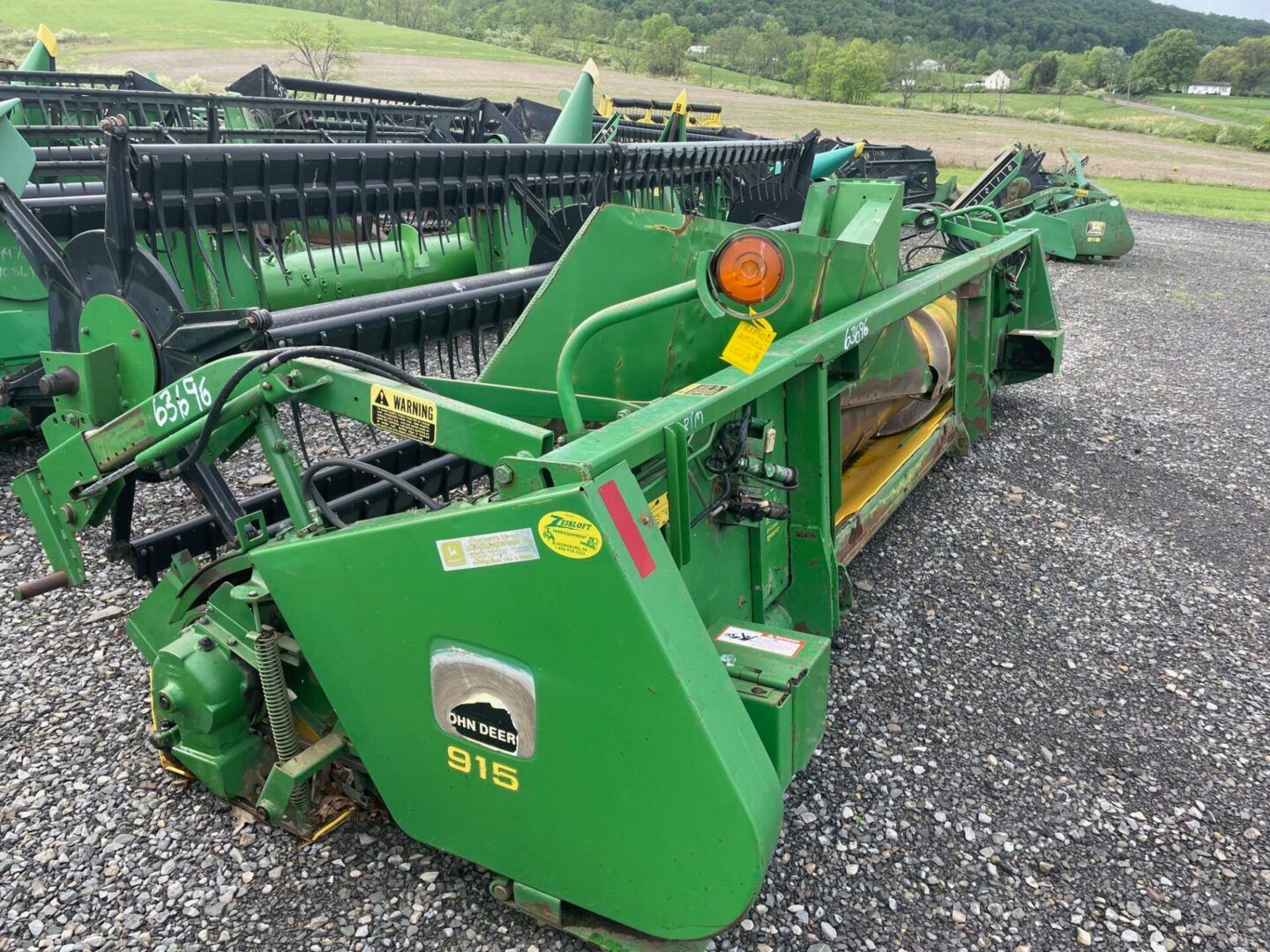 Green agricultural machine on gravel lot with fields in the background