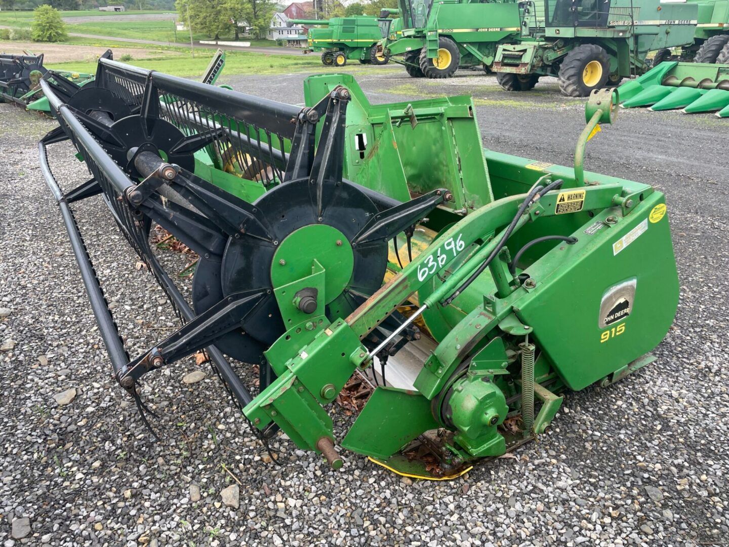 Green farm hay mower on gravel, with black cutting reel and tractor in the background.