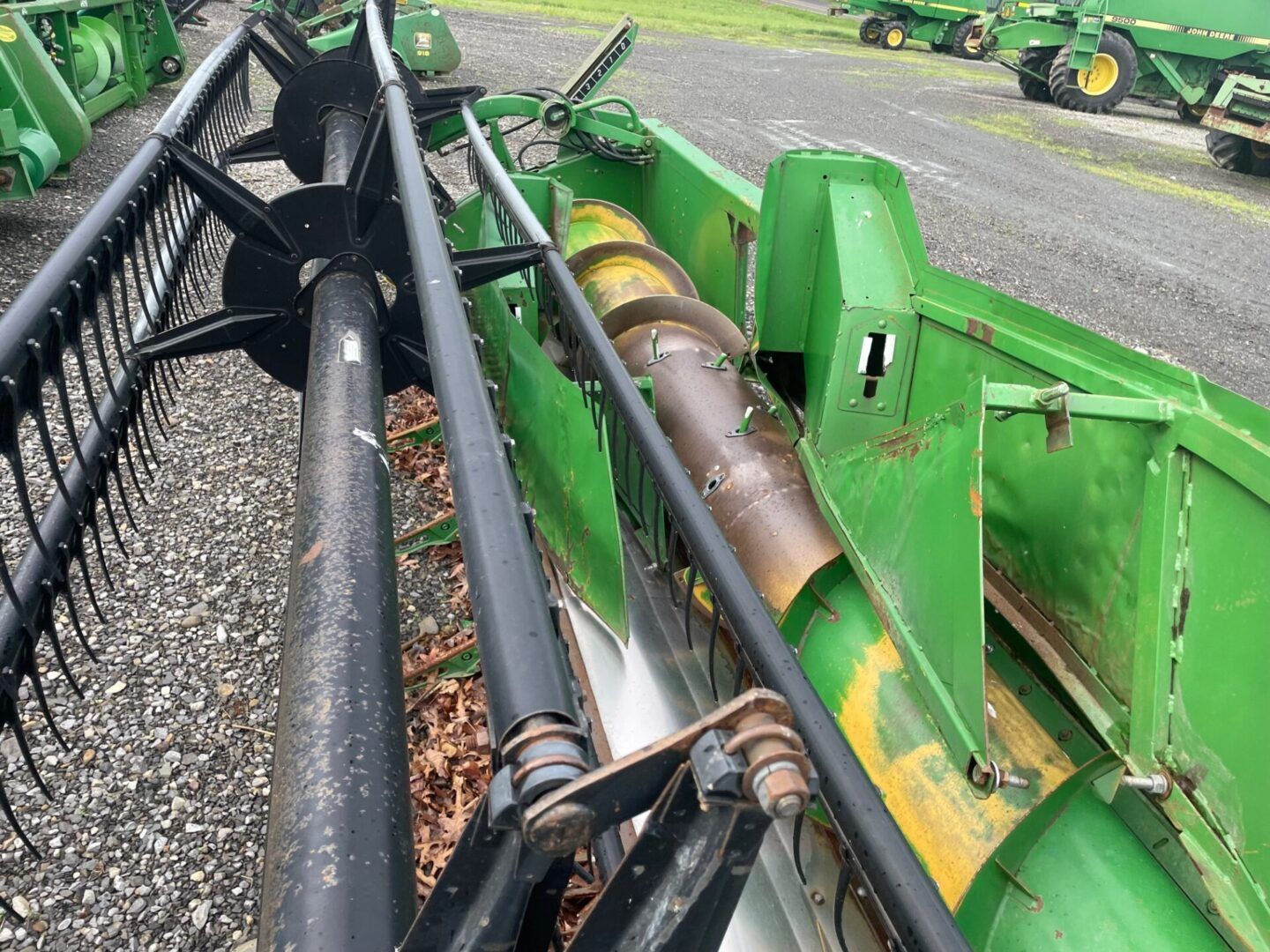 Close-up of green heavy machinery with black hydraulic hoses and metal cylinders on a roadside.