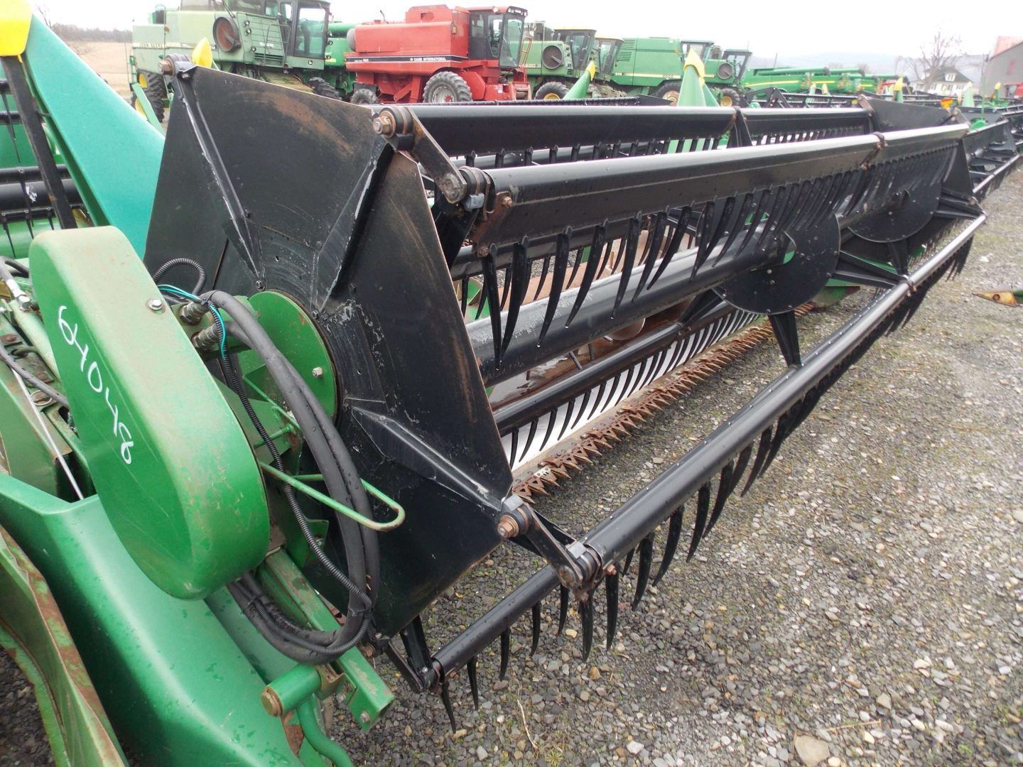 Green combine header with black reel on gravel lot, showing farm machinery close-up