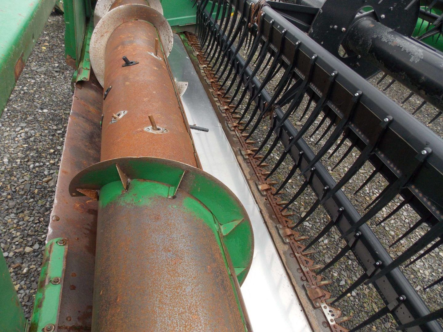 Rusty orange metal pipe beside black conveyor rollers on a gravel surface