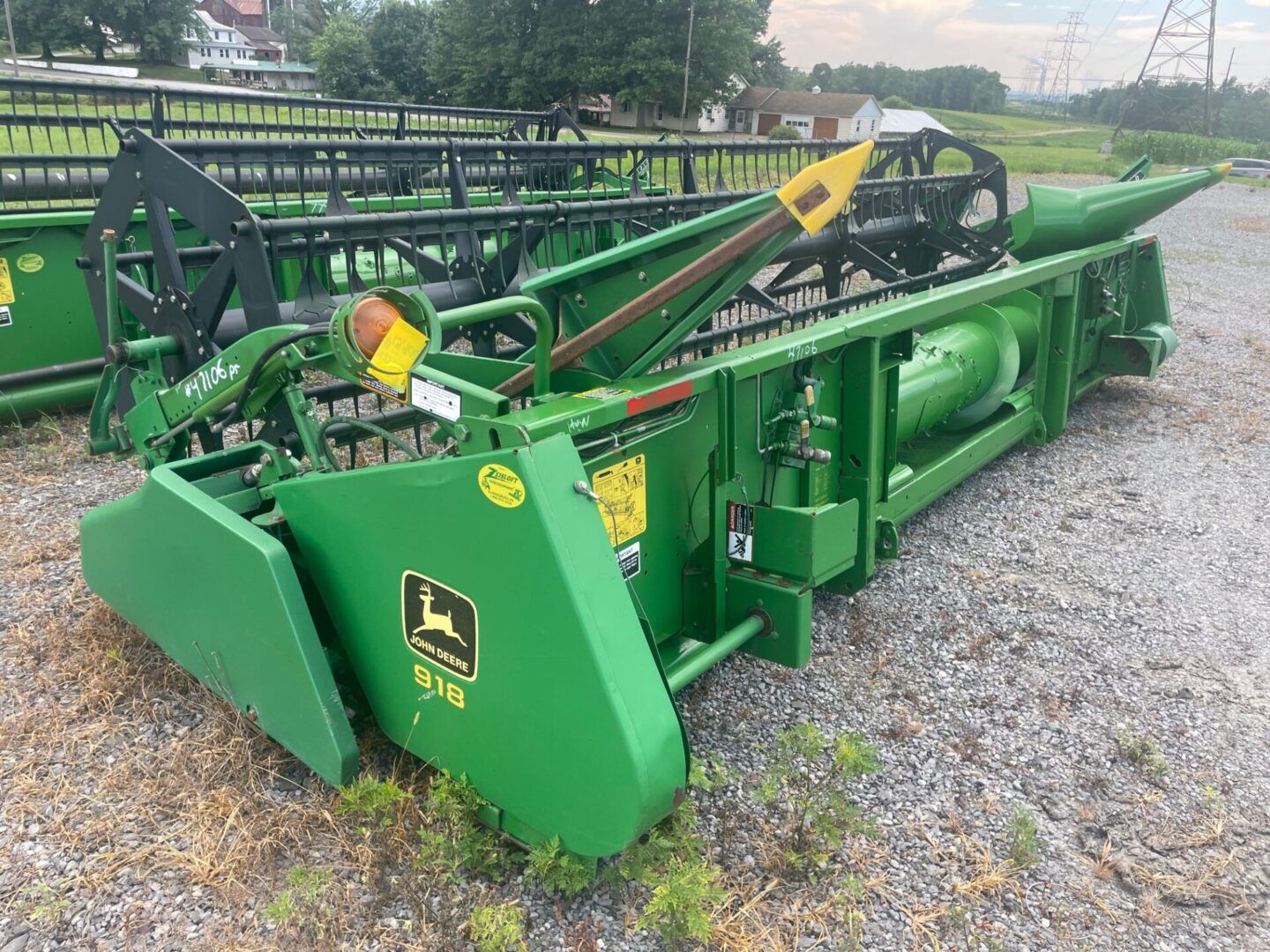 Green John Deere farm mower parked on gravel, with cutting head and metal frame visible.