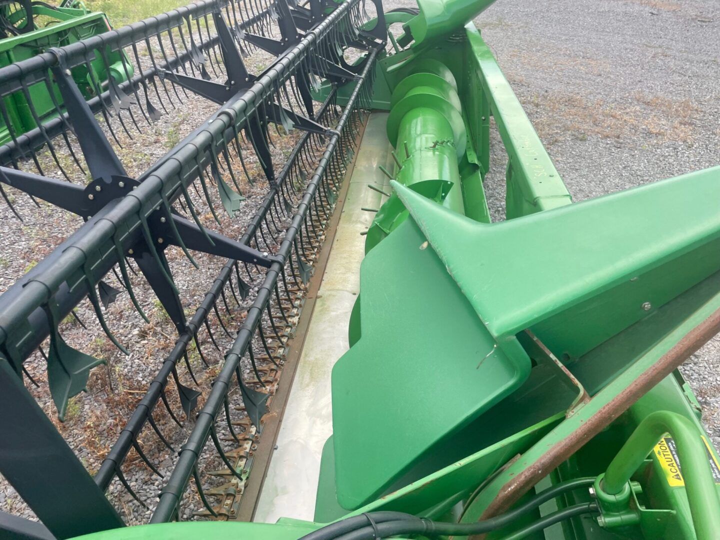 Green tractor attachment beside a black metal fence on gravel