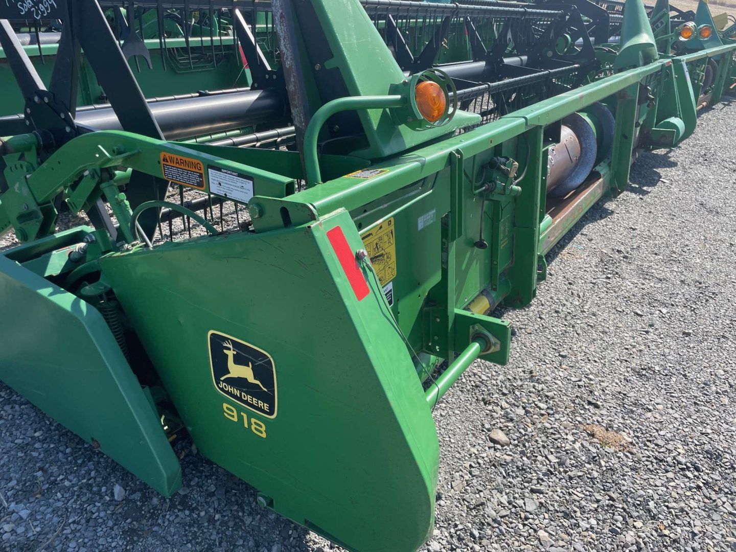 Green John Deere farm attachment on gravel, viewed from the front-left side