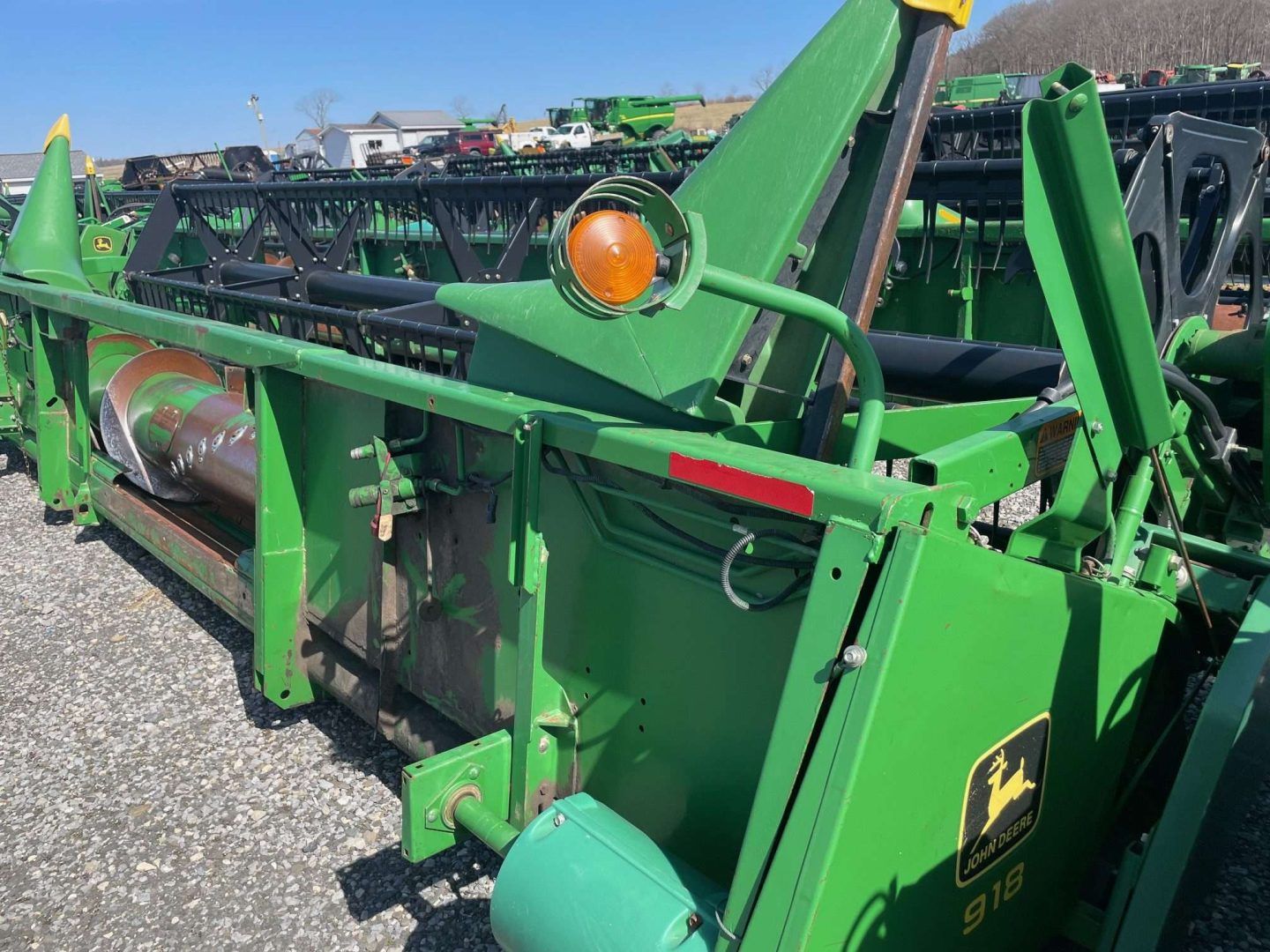 Green John Deere farm equipment parked outdoors on a gravel lot, showing metal arms and orange lights