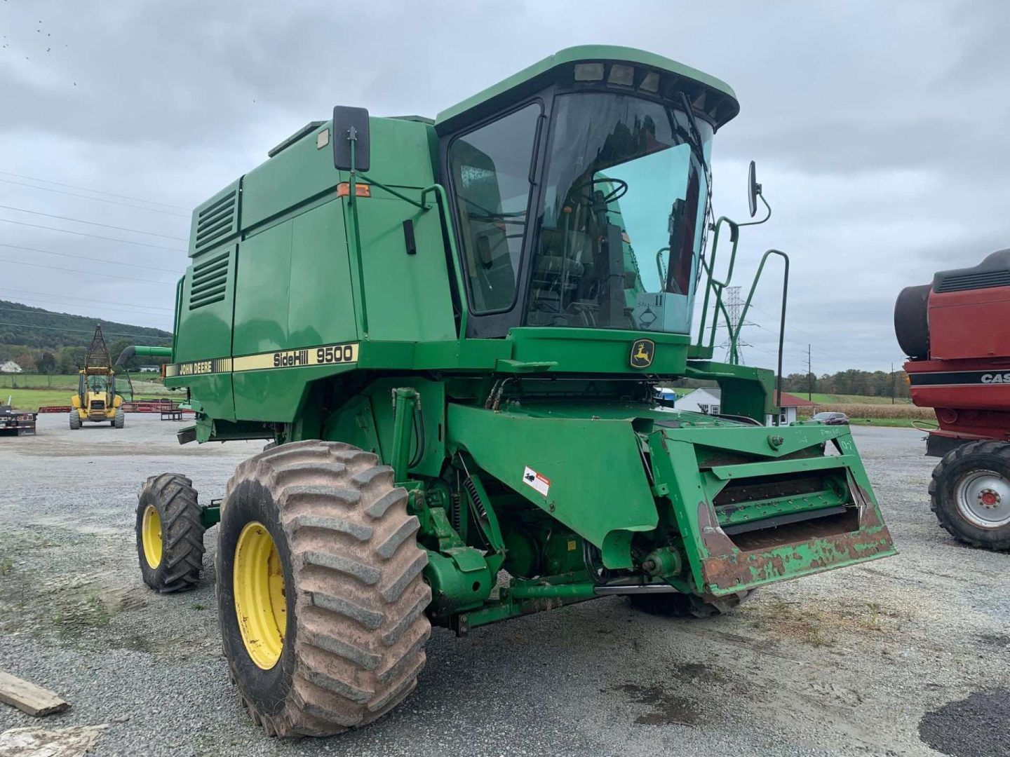 Green John Deere combine harvester parked on a gravel lot under cloudy sky