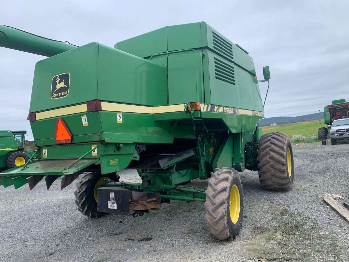 Large green combine harvester on gravel, viewed from rear with yellow-rimmed tires.