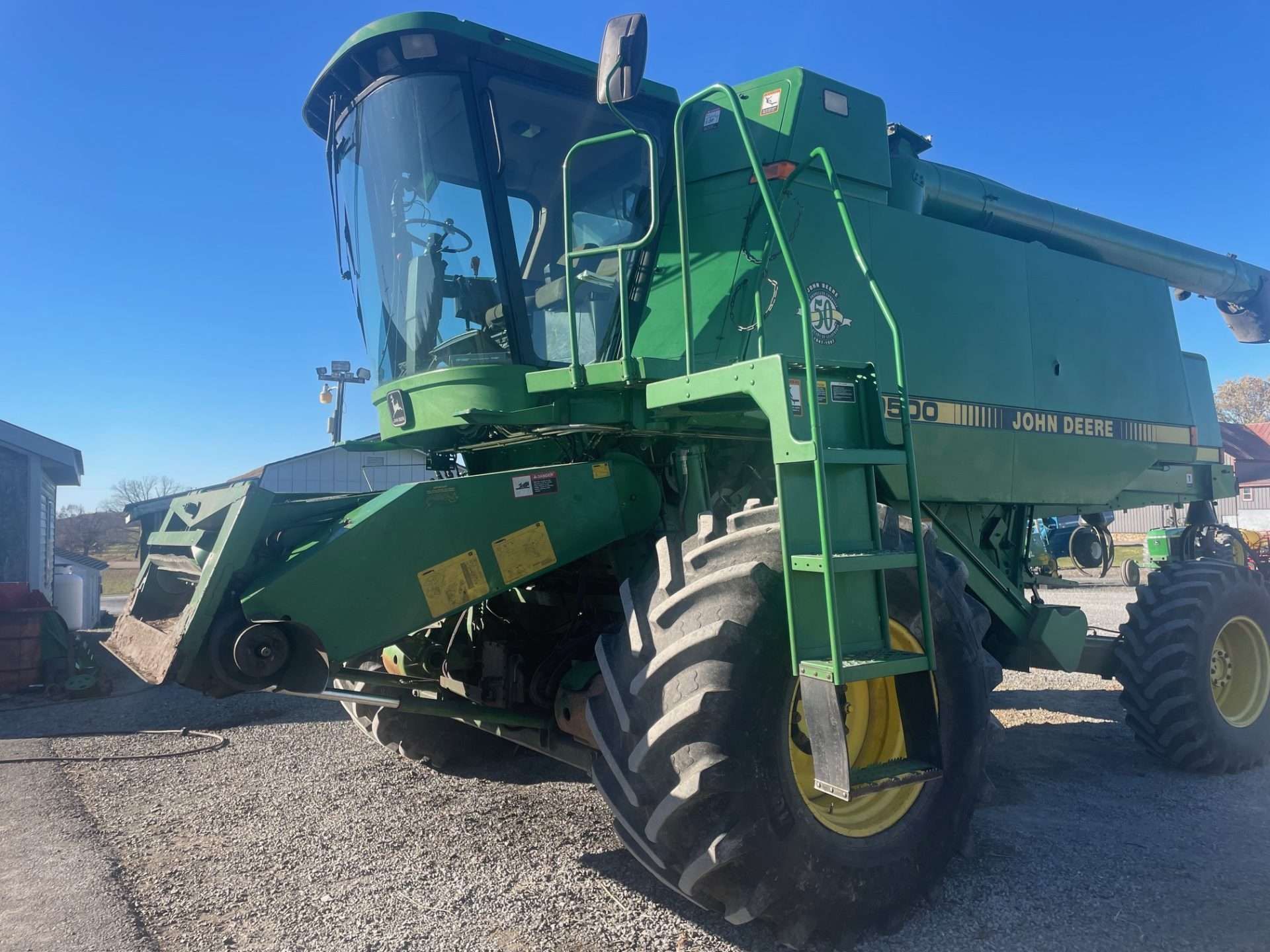 Green combine harvester parked on gravel under a clear blue sky