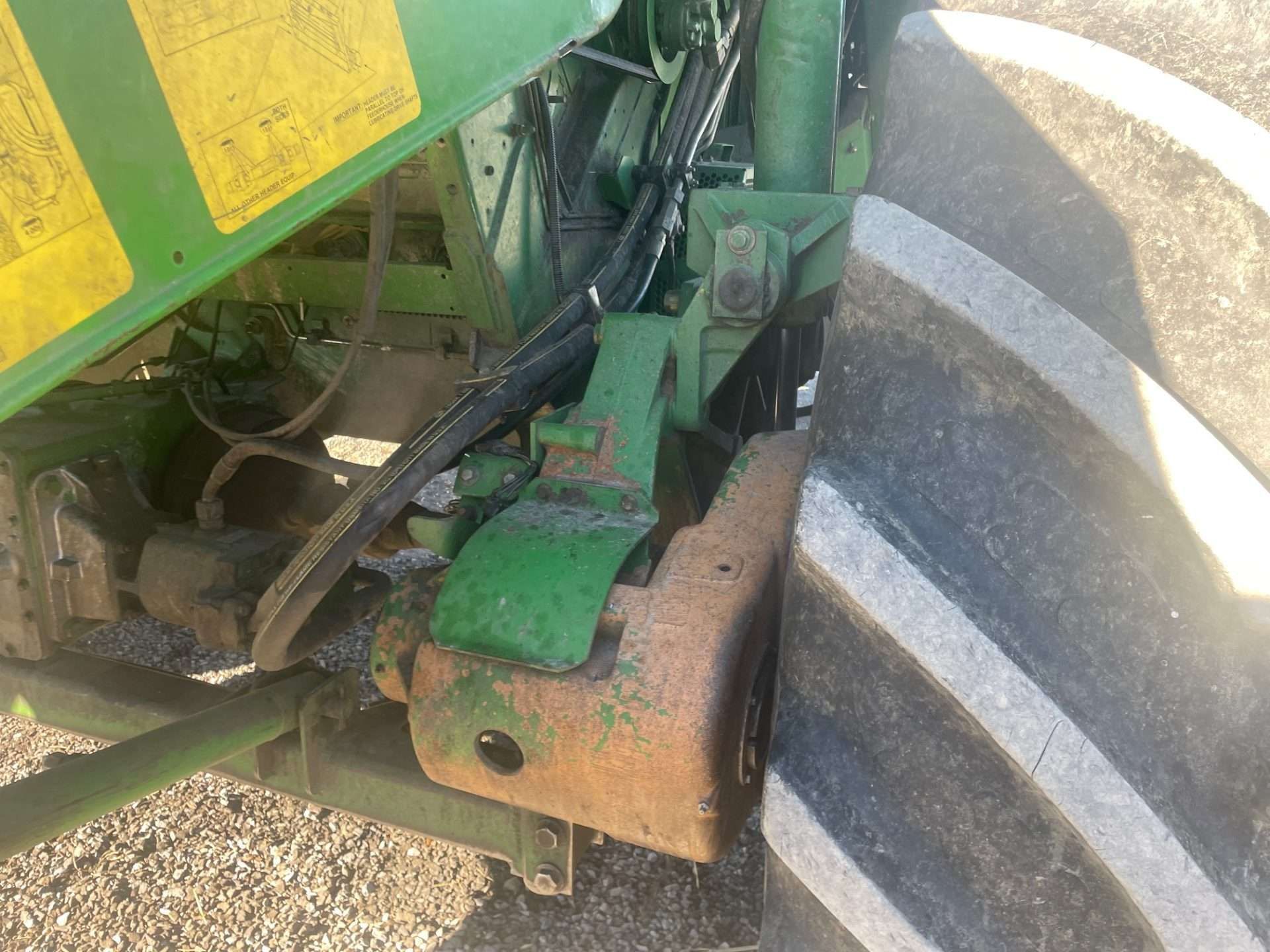 Close-up of a green farm machine’s wheel and metal linkage, with dirt and rust visible.