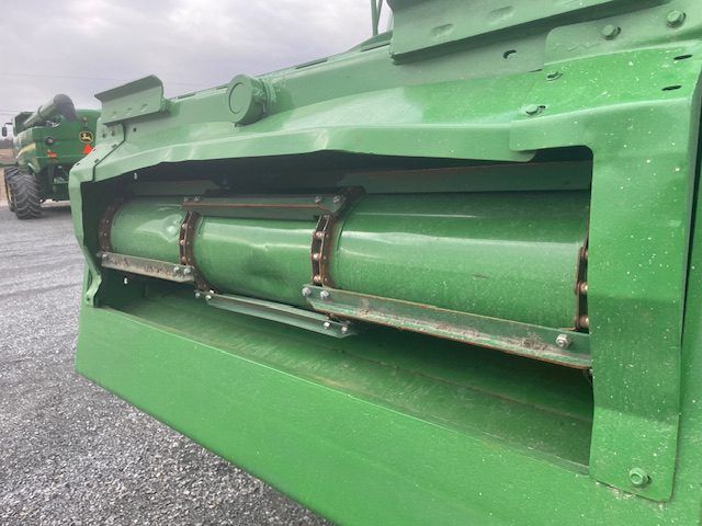Close-up of a green farm machine’s roller mechanism on a gravel lot