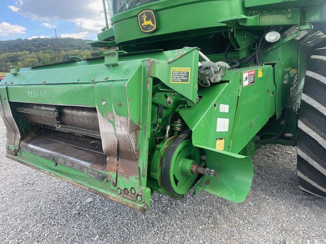 Green John Deere combine harvester header close-up on gravel, with large metal cutting reel and tire visible