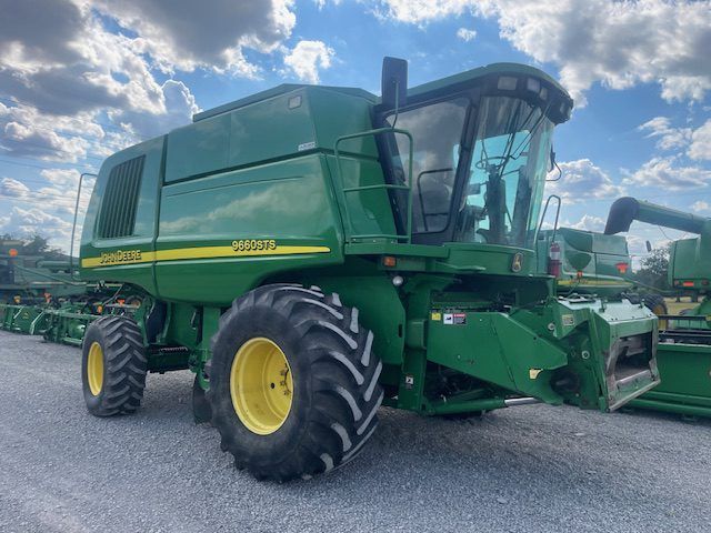 Green John Deere combine harvester parked on a gravel lot under a cloudy sky