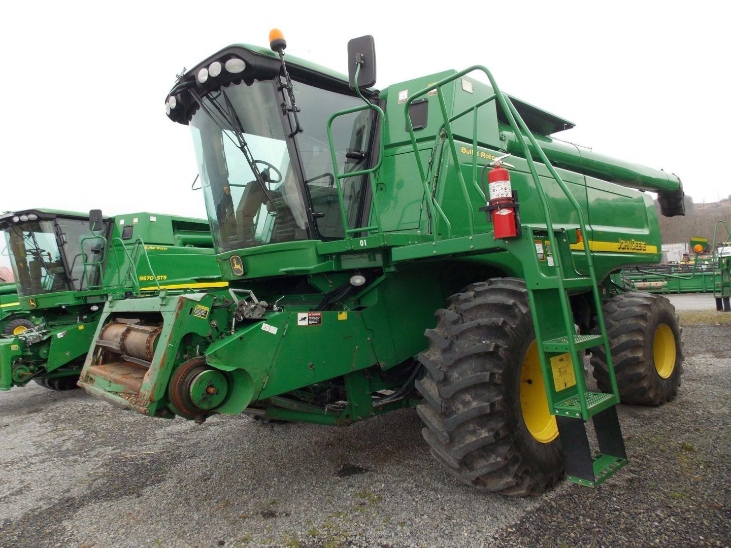 Green combine harvester parked on gravel, with large tires and harvesting header attached