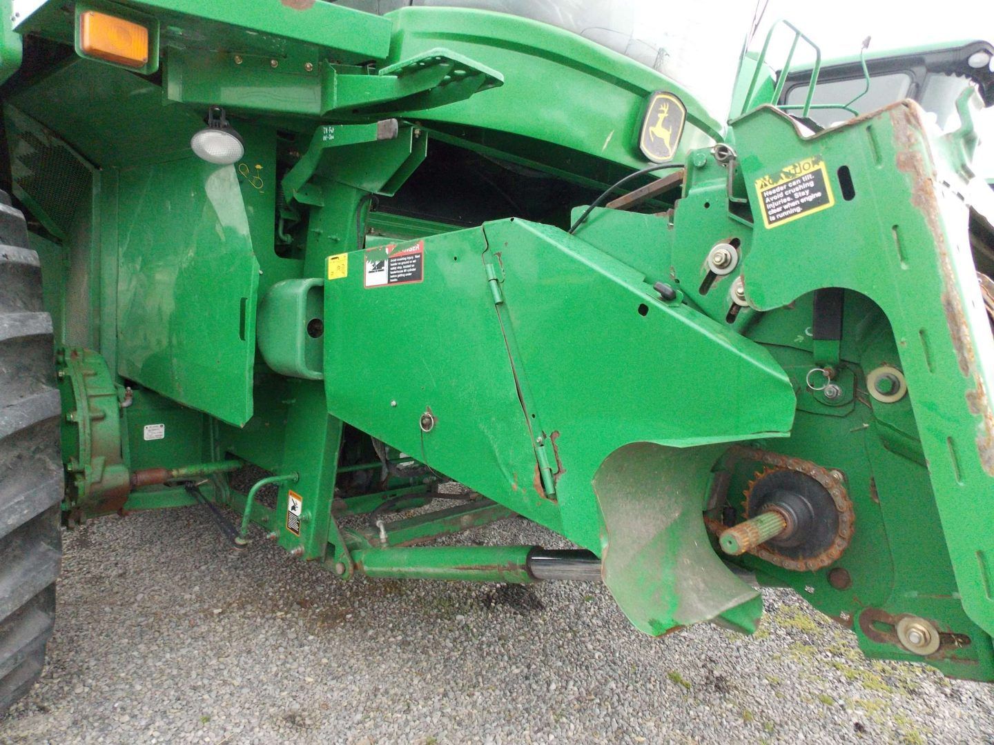 Green agricultural machine parked on gravel, showing its side and front attachment.