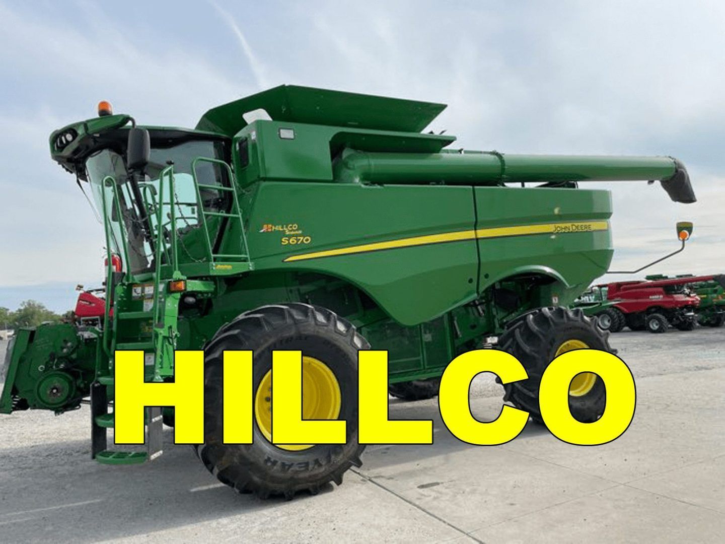 Green combine harvester in a lot, with large yellow “HILLCO” text overlaid