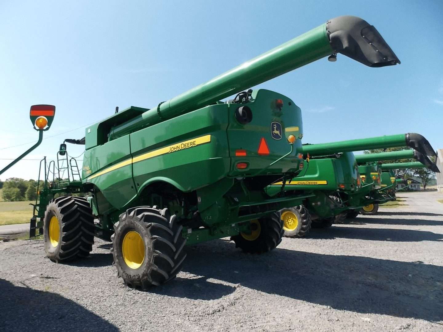Green combine harvesters parked on a gravel lot under a clear blue sky