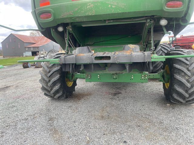 Low-angle view of a green tractor’s rear wheels and undercarriage on a gravel driveway.