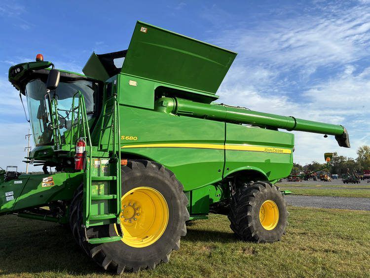 Green combine harvester with yellow wheels in a field under a blue sky