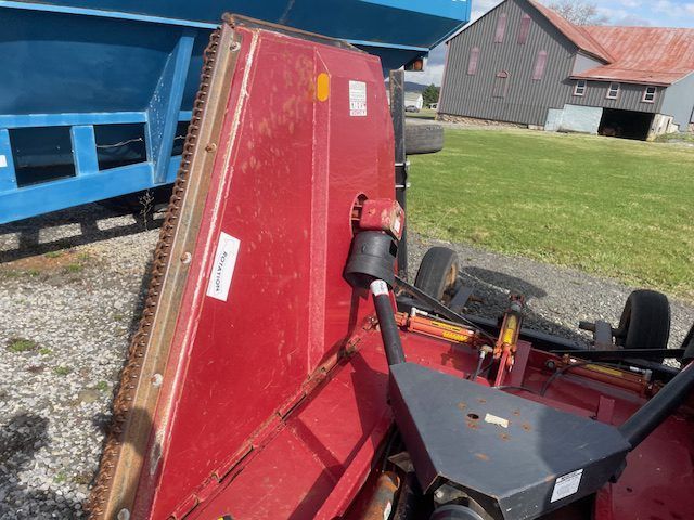 Overturned red mower deck beside a blue trailer and a barn in a grassy yard