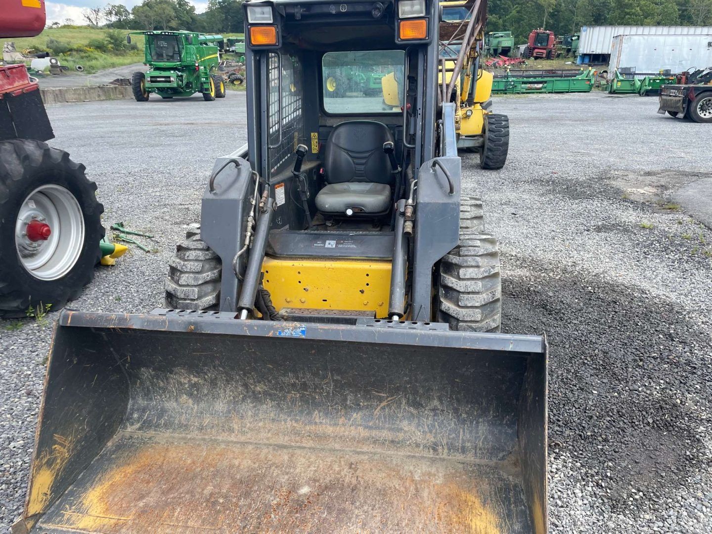 Small skid steer loader with front bucket on a gravel lot, viewed from the front.