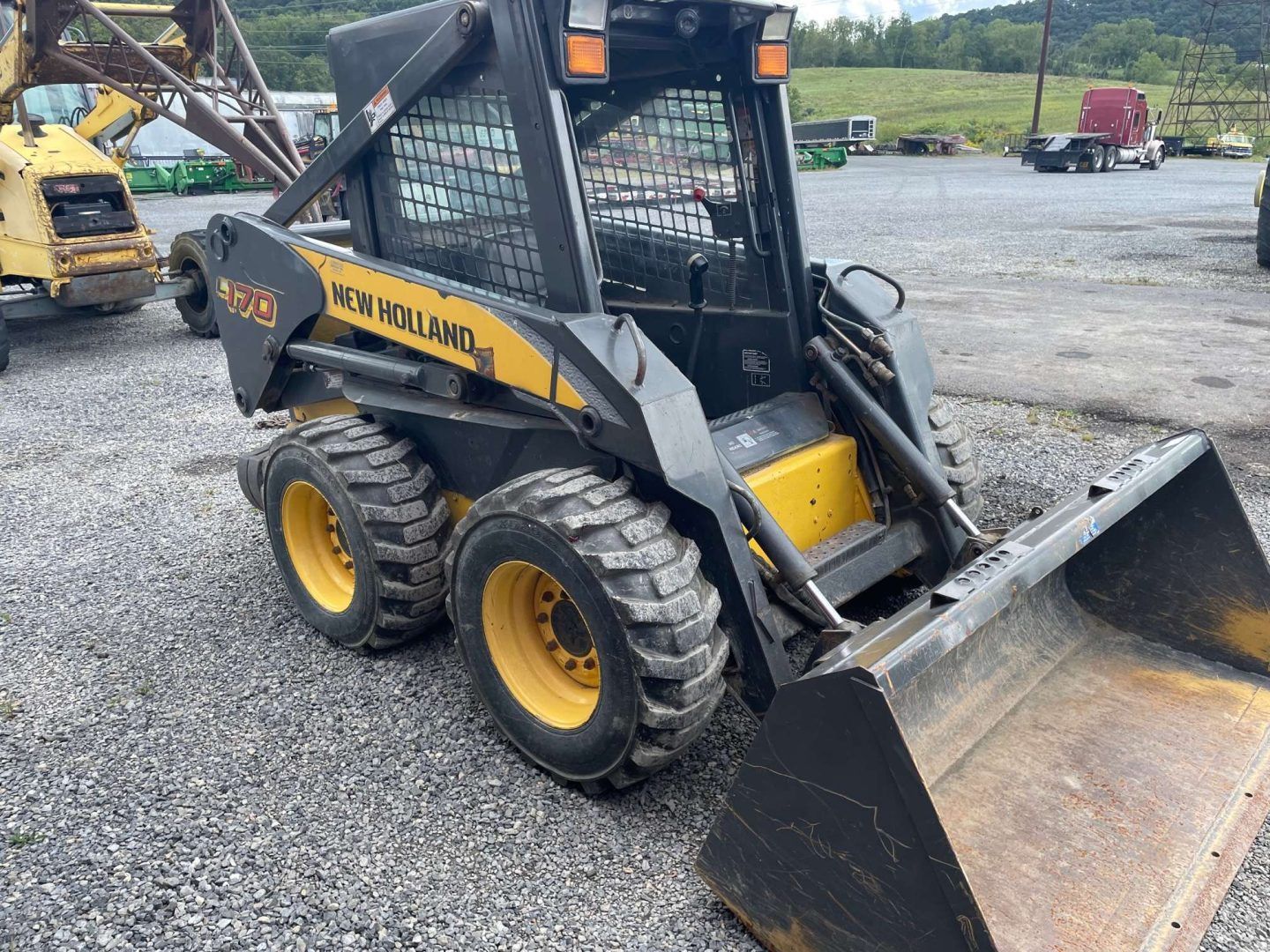 Yellow skid steer loader with front bucket on a gravel lot, viewed from the side