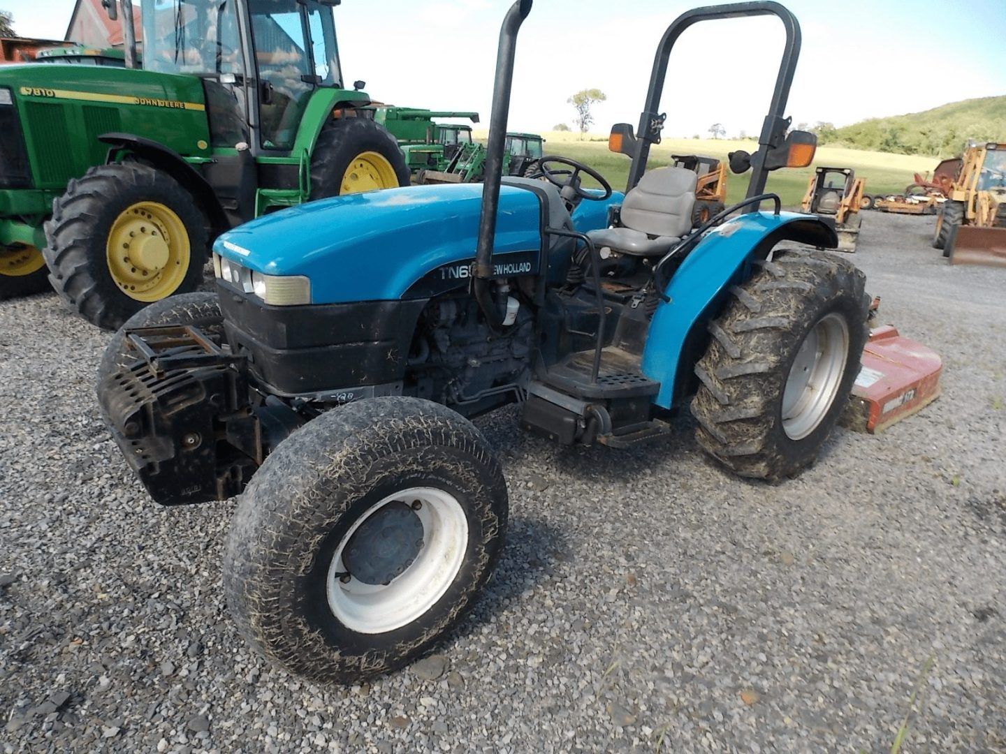 Blue compact tractor parked on gravel with a green tractor in the background