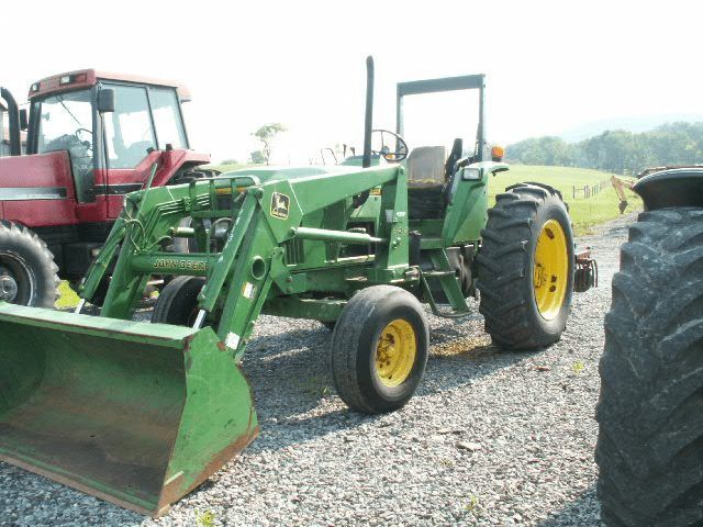 Green tractor with front loader parked on gravel beside a red tractor in a field
