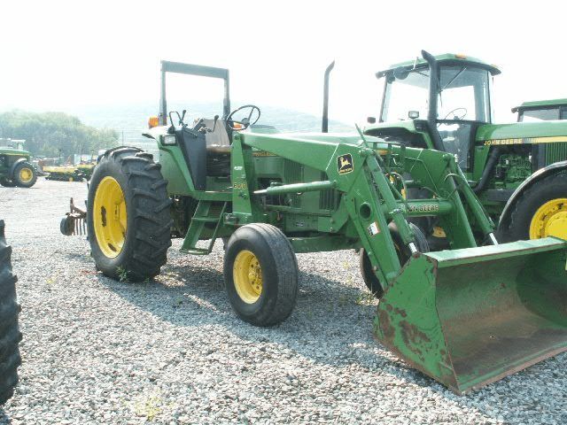 Green tractor with front loader parked on gravel lot, other tractors in background