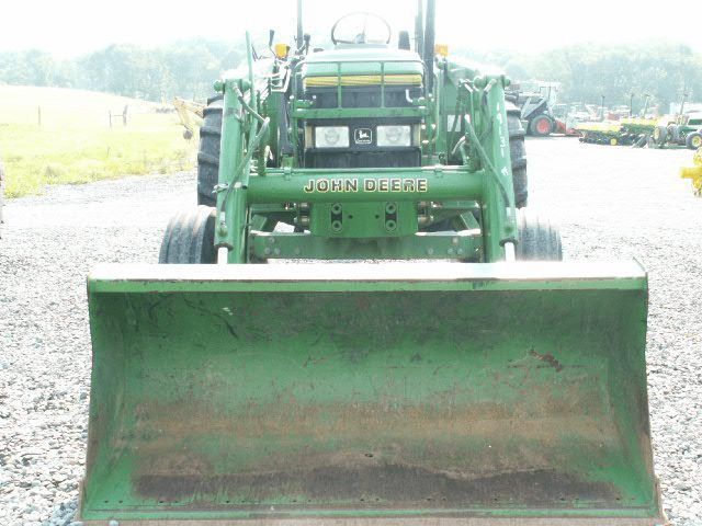 Green tractor with a front loader parked on a wet road in a rural area.