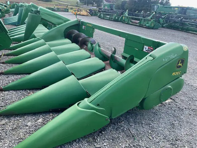 Large green agricultural equipment lined up outdoors on gravel near a farm building.