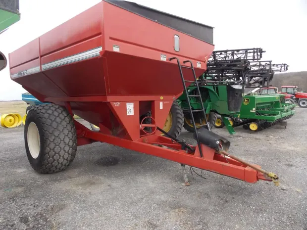 Red grain cart with large tires parked on gravel at an equipment lot