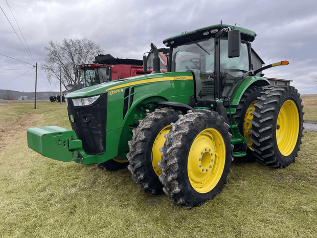 Green John Deere tractor with yellow wheels parked in a grassy field under a cloudy sky