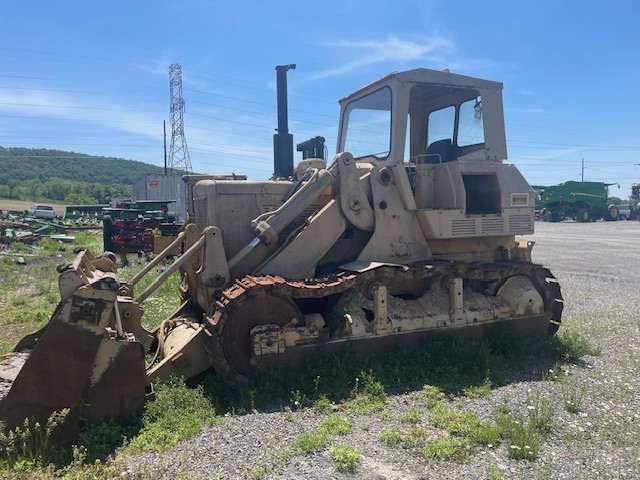 Old tracked bulldozer with front blade parked in a gravel lot under a blue sky