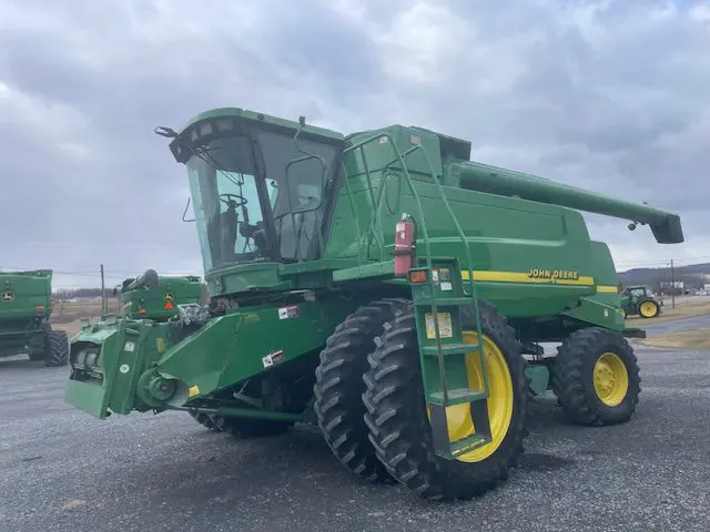 Green combine harvester parked on gravel under a cloudy sky