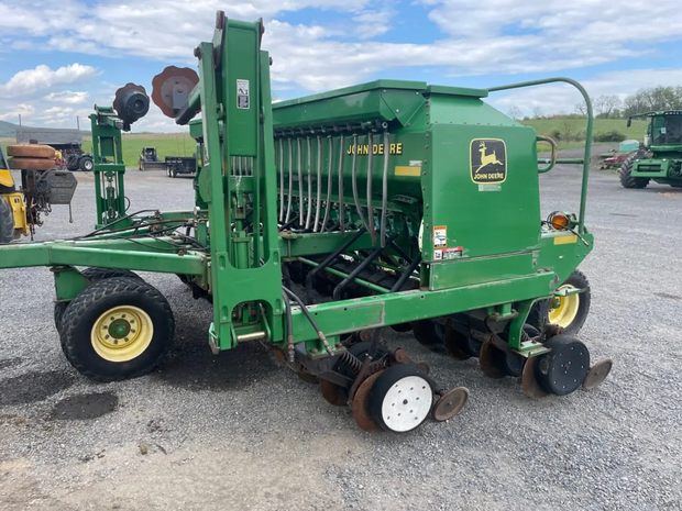 Green John Deere farm machine on gravel lot, with wheels and attached harvesting equipment.