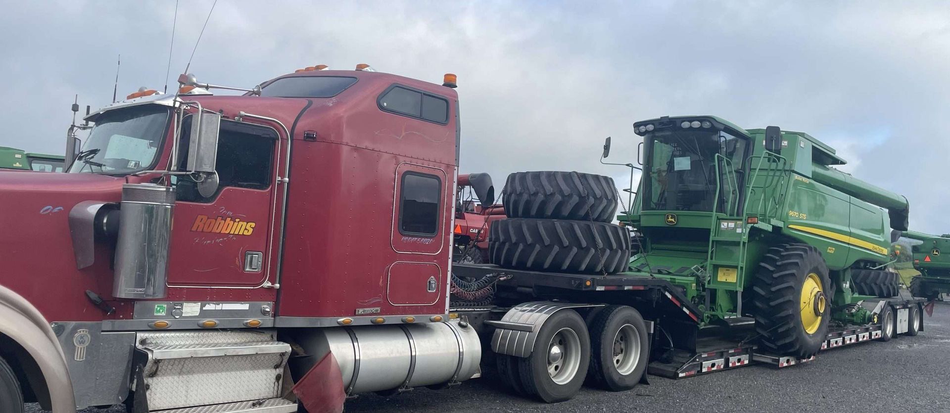 Red semi truck hauling a green combine harvester on a flatbed trailer on a road