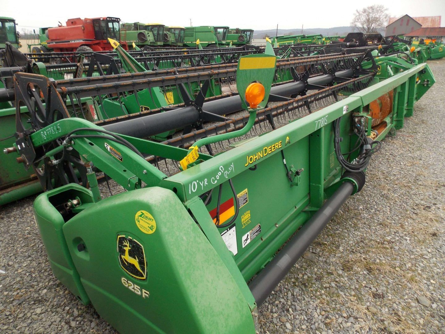 Green John Deere farm header equipment lined up on a gravel lot.