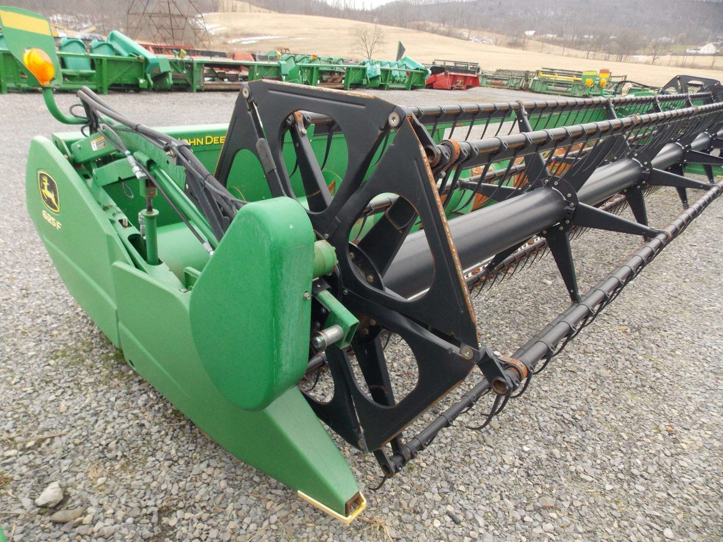 Green farm combine header with black reel parked on gravel outdoors