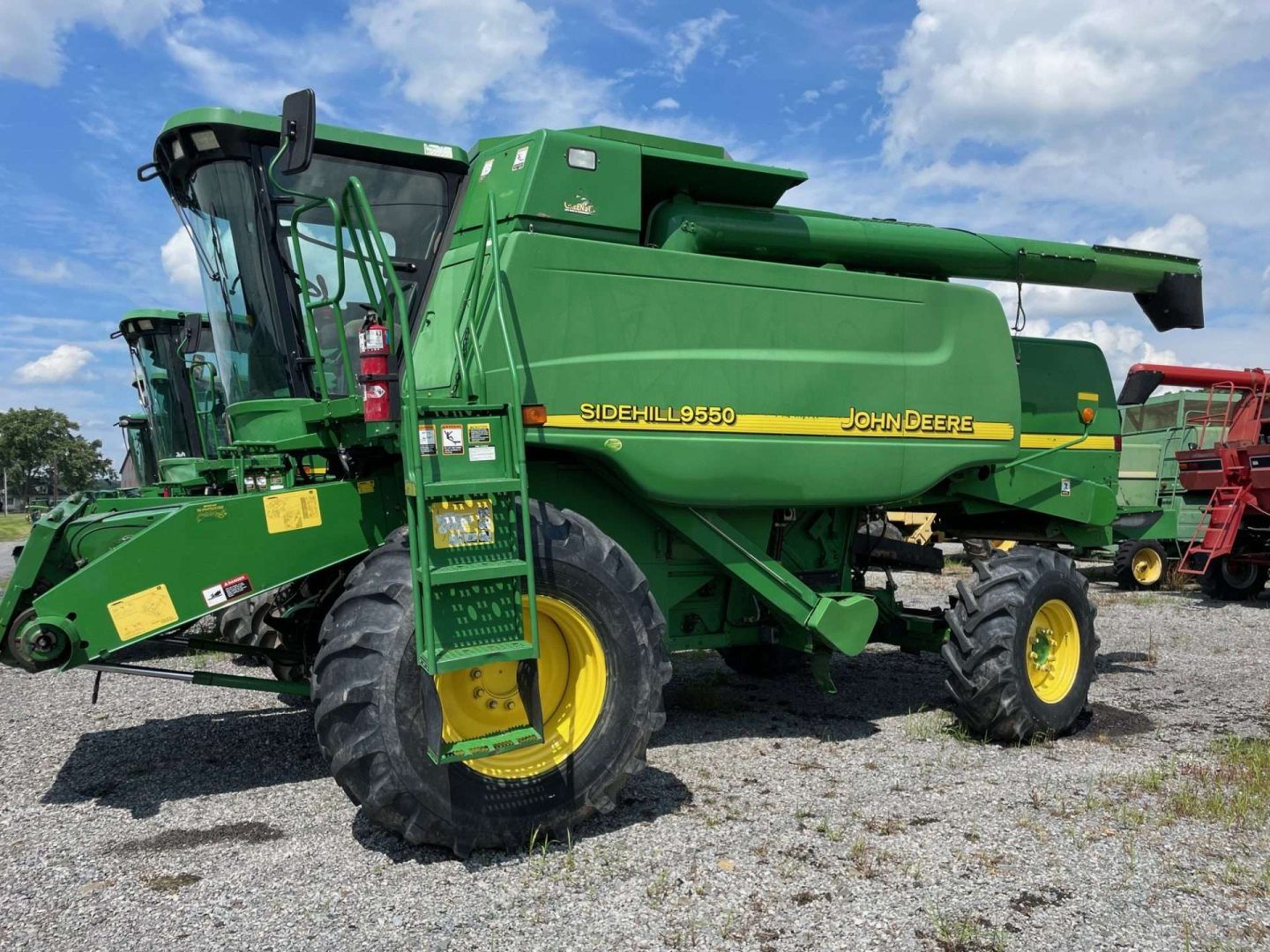 Green John Deere combine harvester parked on gravel under a blue sky with clouds